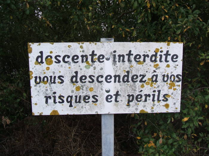 Danger sign along the cliff face near Pointe du Hoc: Access Interdite.  Vous descendez a vos risques et perils.