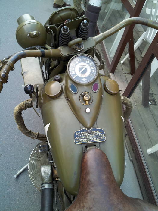 A vintage U.S. military Harley-Davidson motorcycle with a Belgian license plate outside a brasserie in Sainte-Mère-Église.