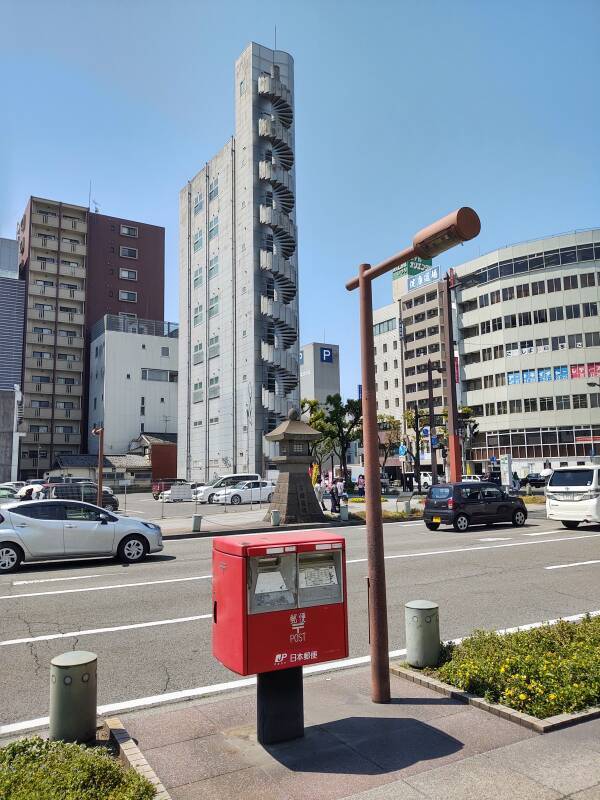 A red mailbox in front of a narrow tower.