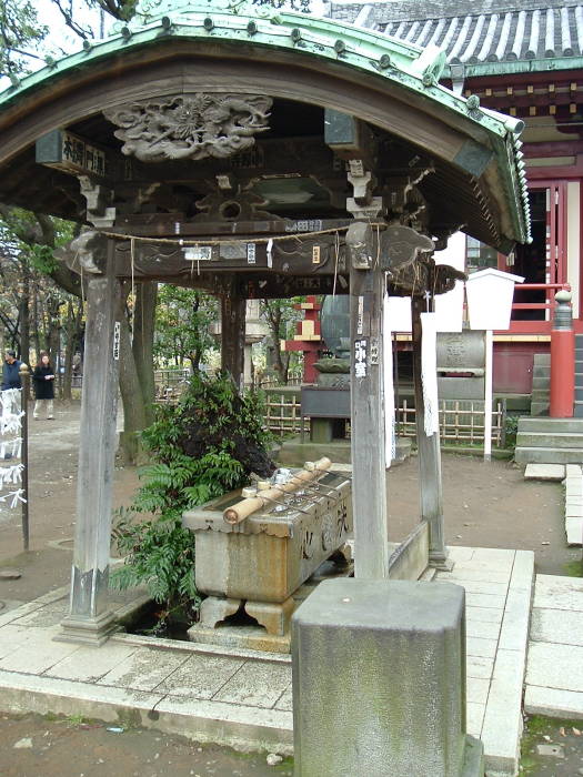 Chōzuya, or ritual water trough at Benzaiten Buddhist Temple in Tōkyō. Metal ladles rest on a bamboo shaft. The ladles are used for ritual washing before entering the temple.