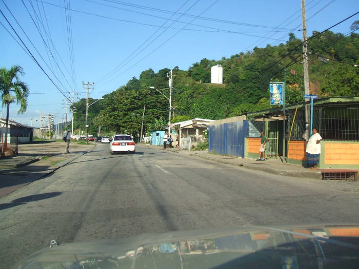 Driving along a two-lane road, leaving the Trinidadian village of Carenage and approaching the sea.