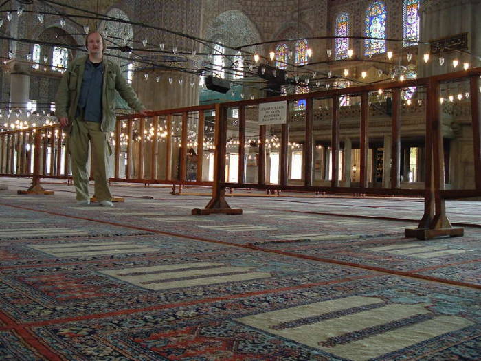 Interior of the Blue mosque or Sultanahmet Cami, in Istanbul.  Mihrab and Minbar.  Large chandeliers above many prayer rugs.