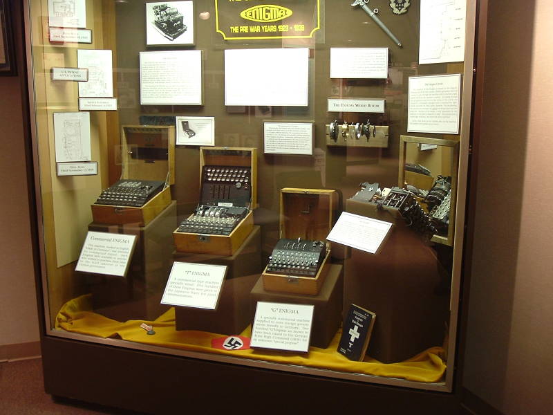 Museum case displaying several Enigma machines: Commercial Enigma machine; 'T' Enigma, a modified commercial unit given to the Japanese Navy; 'G' Enigma, modified 4-rotor unit supplied to foreign governmnets friendly to Nazi Germany; disassembled rotor and Enigma removed from its case.