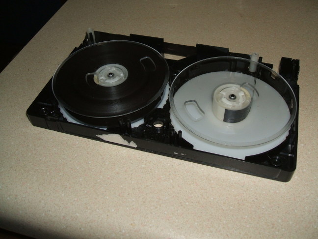 VHS tape split open, tape threaded manually.