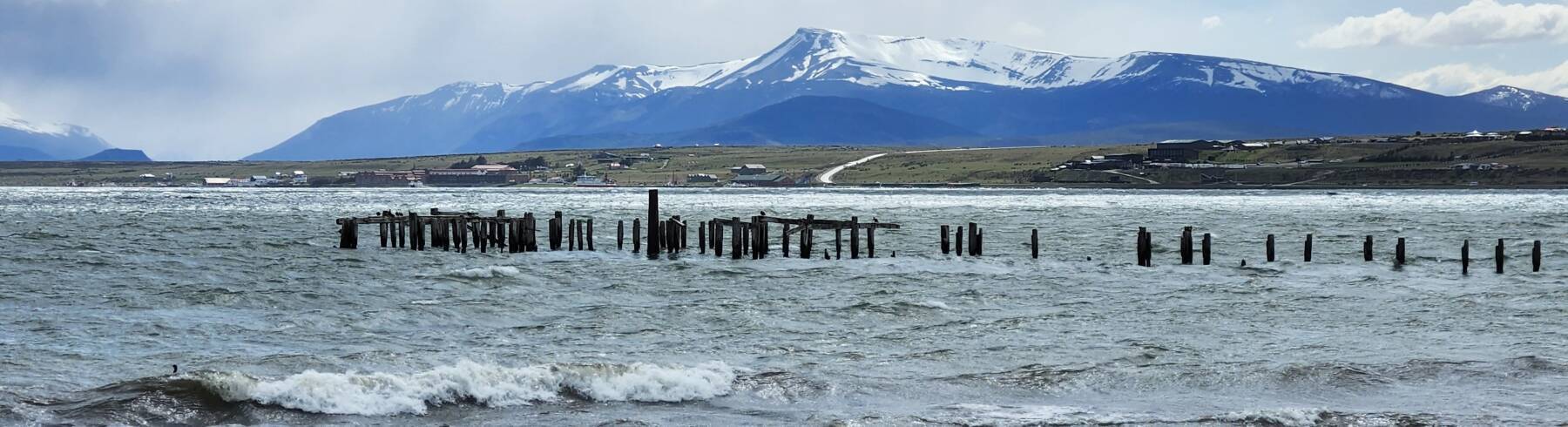 View northwest across Golfo Almirante Montt from waterfront of Puerto Natales to Puerto Bories and snow-covered mountains beyond.