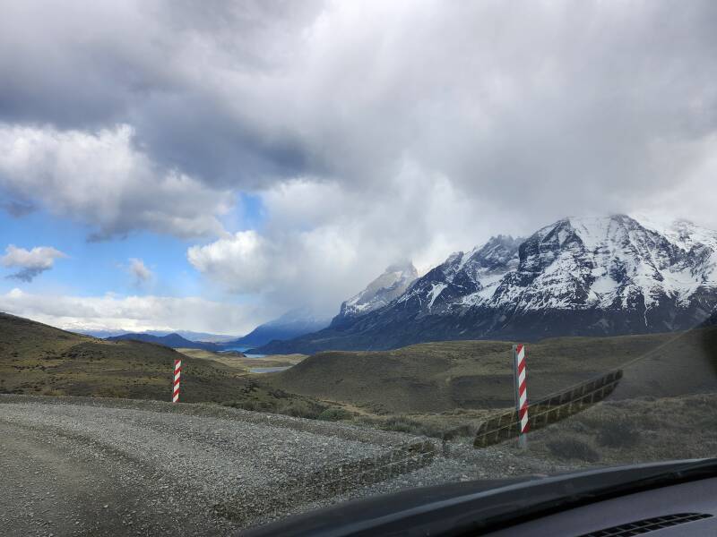 View out the windshield over Lago Nordenskjöld with Cerro Ferrier in the distance. To the right are, far to near: Cerro Paine Grande mostly obscured by clouds, Cuernos del Paine, and Monte Almirante Nieto