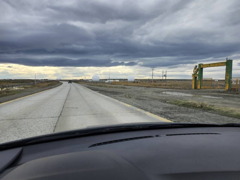 Two-lane highway past an entrance to an industrial facility and several large white radomes.