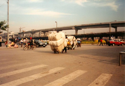 Man pulling an enormous wheelbarrow down a road in China.