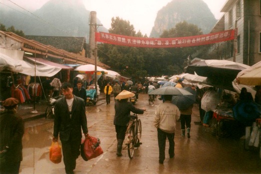 People carrying packages, woman in a conical straw hat, market day in Yangshuo, China.