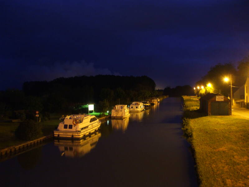 Canal boats tied up at Beaulieu-sur-Loire with lights of the nuclear power plant in the distance.