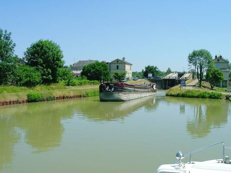 Large commercial barge exiting the high double lock and canal bridge at Guétin.