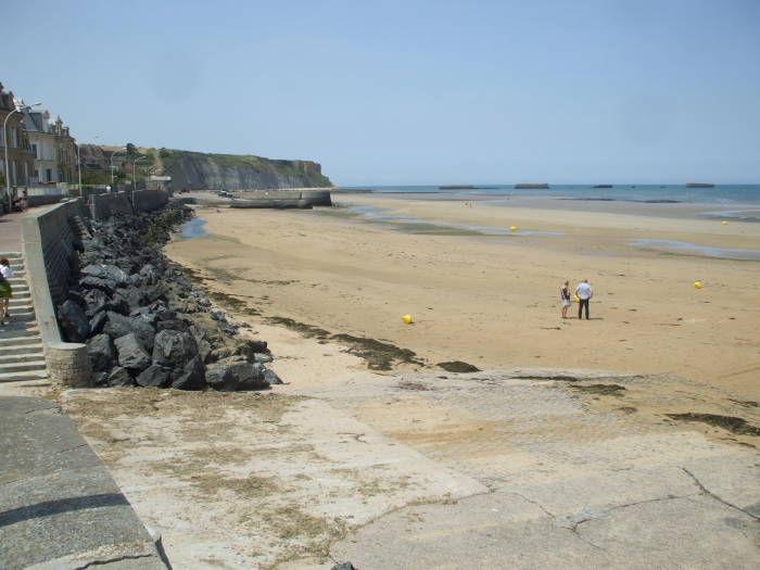 The harbor at Arromanches at low tide.  Mulberry artificial harbors from D-Day are visible in the bay.  Cliffs in the distance