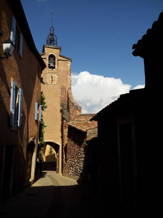A clock tower spans a small back street in Roussillon.