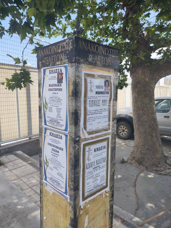 Pillar with several funeral notices, at night along a street in Sitia.