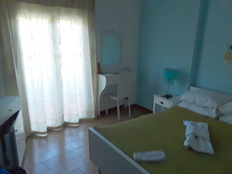 Interior of hotel room in Alinda: bed, night table, desk, refrigerator.