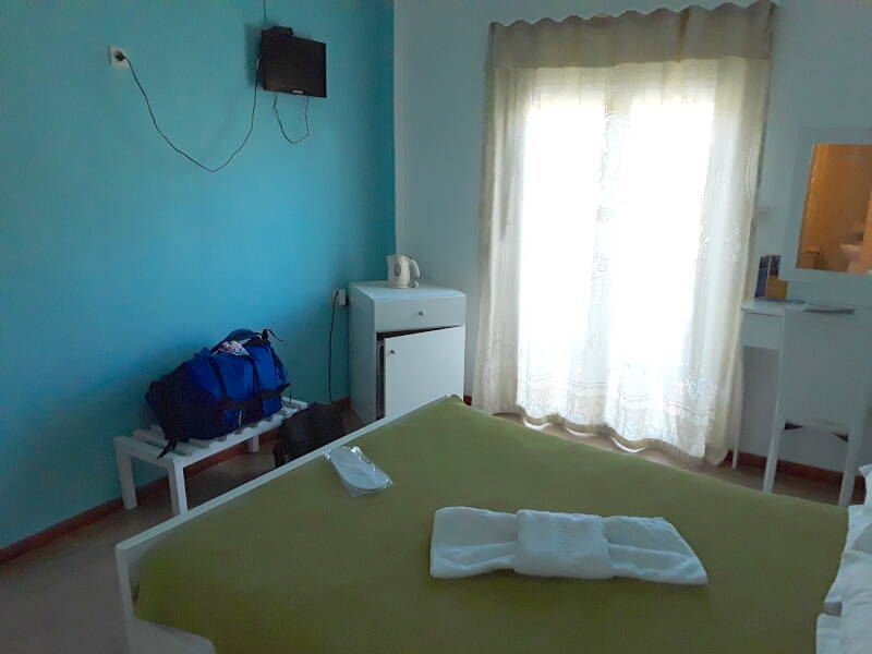 Interior of hotel room in Alinda: bed, desk, refrigerator, television.