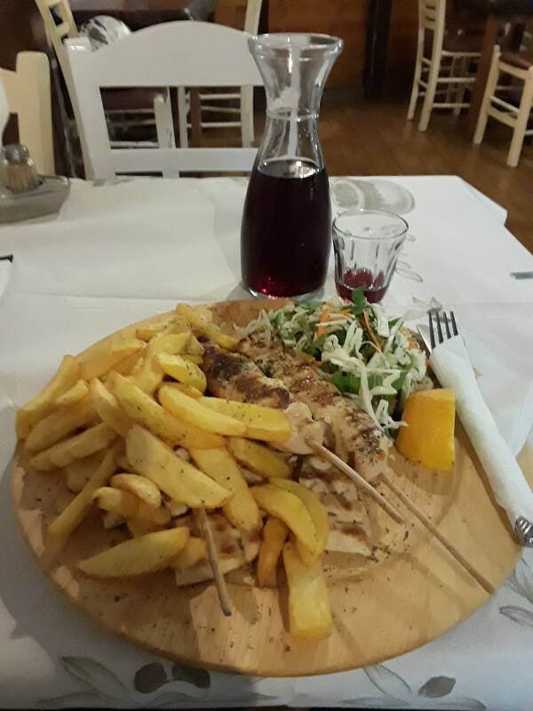 Chicken souvlaki with salad, pita, and french fried potatoes, with a half-liter of red wine in Alinda.