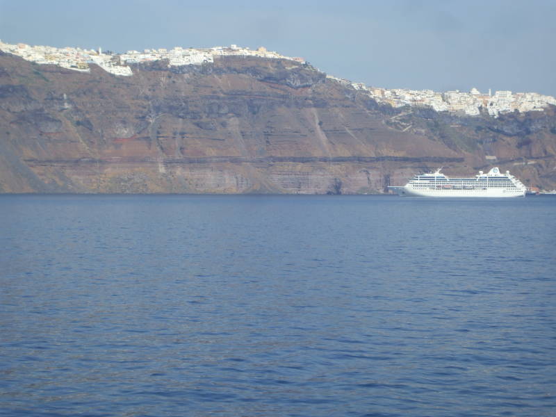 Fira on Santorini, on top of the 300 meter high cliffs above the central caldera, with a large cruise ship in the foreground.