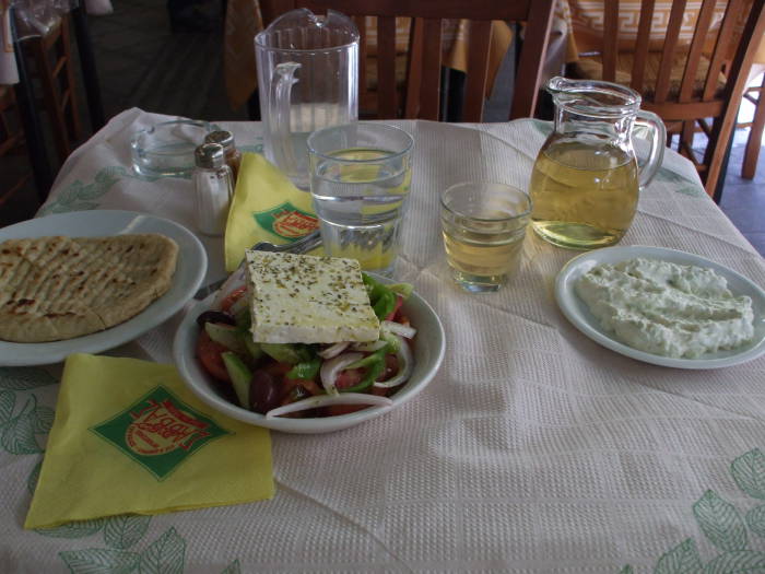 Table of Greek food: Country salad (horiatiki salata), pita, tzatziki, and retsina.