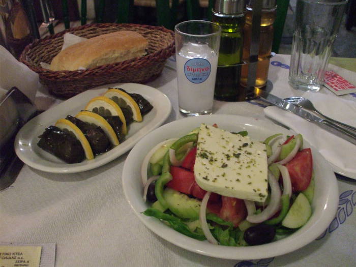 Greek village salad or horiatiki and dolmades or stuffed grape leaves, and a glass of ouzo, in a Greek taverna in the Plaka district in Athens.