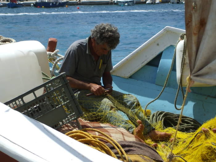 Fisherman repairing his nets in the harbor on Ios island.