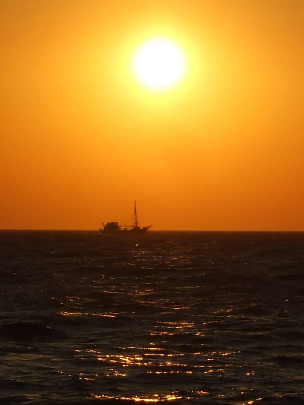 Fishing boat crosses in front of the setting sun, as seen from Mykonos.