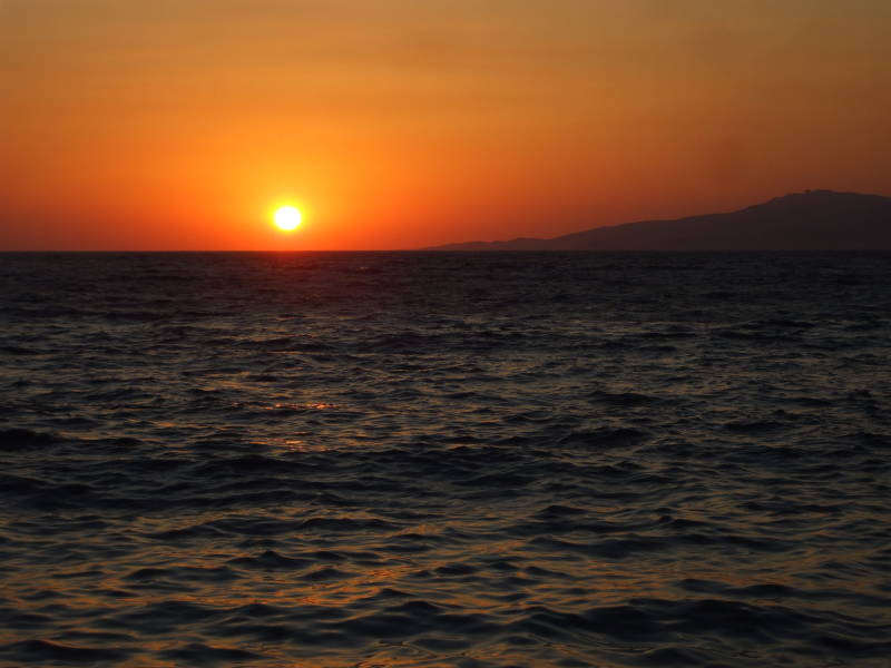 The sun sets into the Aegean near the island of Tinos, as seen from Little Venice in Hora, on Mykonos.
