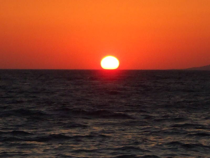 The sun sets into the Aegean near the island of Tinos, as seen from Little Venice in Hora, on Mykonos.