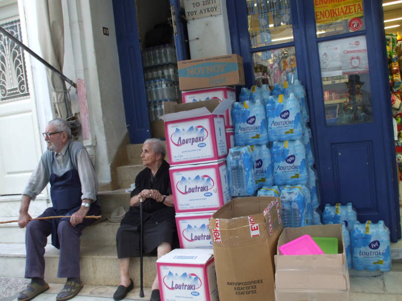 A local couple sits on their steps and watches the tourists walk past on Matogianni, the main street south through Hora on Mykonos.