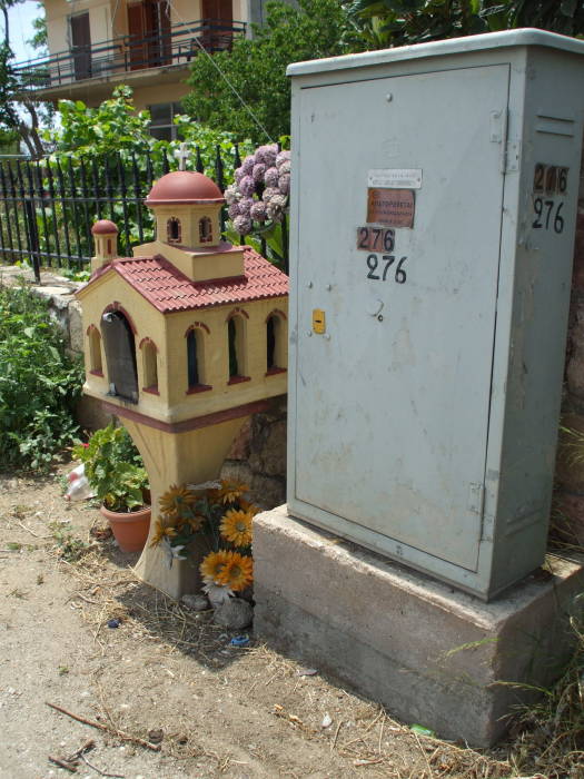 Greek Orthodox shrine, telecommunications cabinet, and potted plants outside Nafplio.
