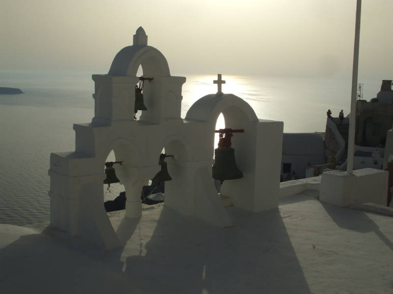 Sunset behind church bells in Oia, a small town on the Greek island of Santorini.