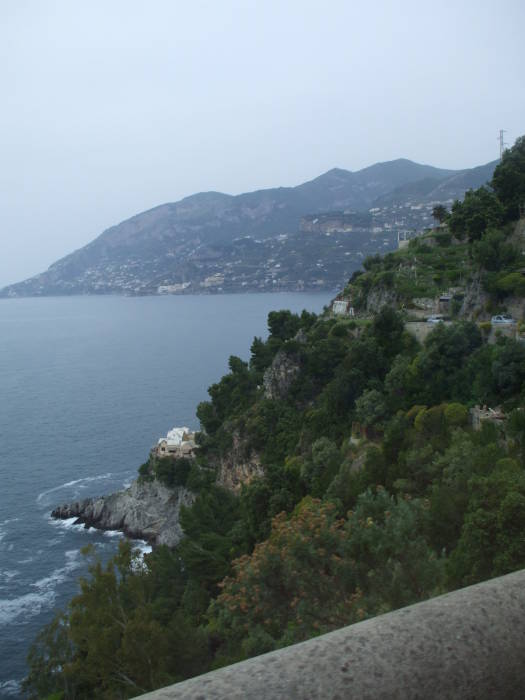 A view from the crowded bus window over the low guardrail, looking back along the rugged coastline.