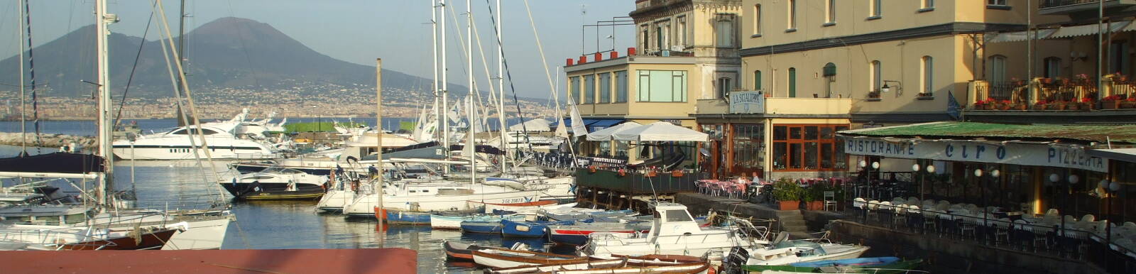 Mount Vesuvius across Naples harbor above sailboats and waterfront cafes.