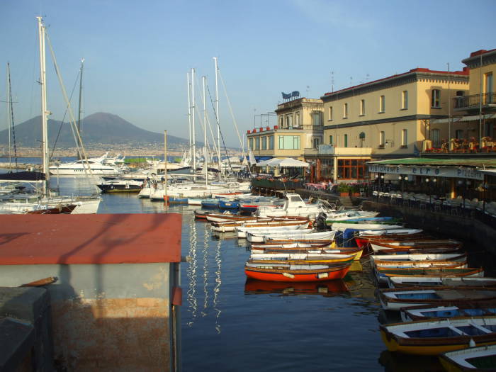 Mount Vesuvius across Naples harbor above sailboats and waterfront cafes.