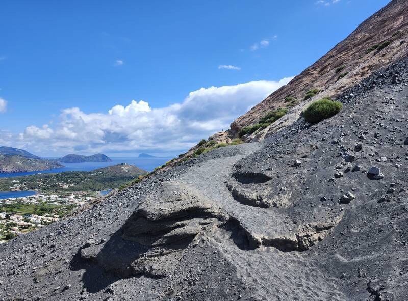 Path crosses from dark coarse sand to compacted ash.