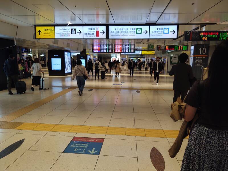 Crowds of people moving through Tōkyō Station, sign pointing to Shinkansen tracks.