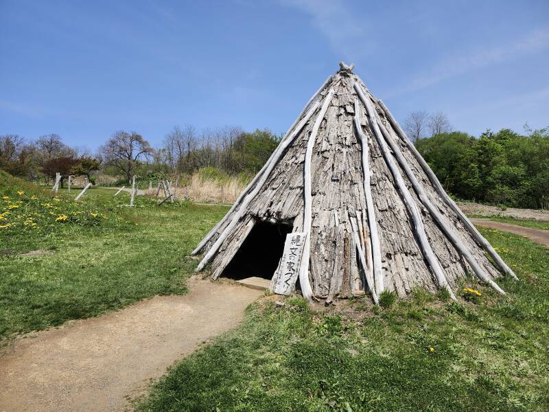 Reconstructed conical dwelling built from wood poles and bark pieces.