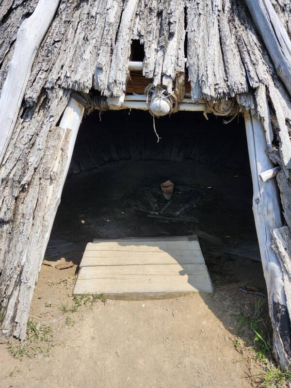 Entryway to conical structure built from wood poles and bark pieces.