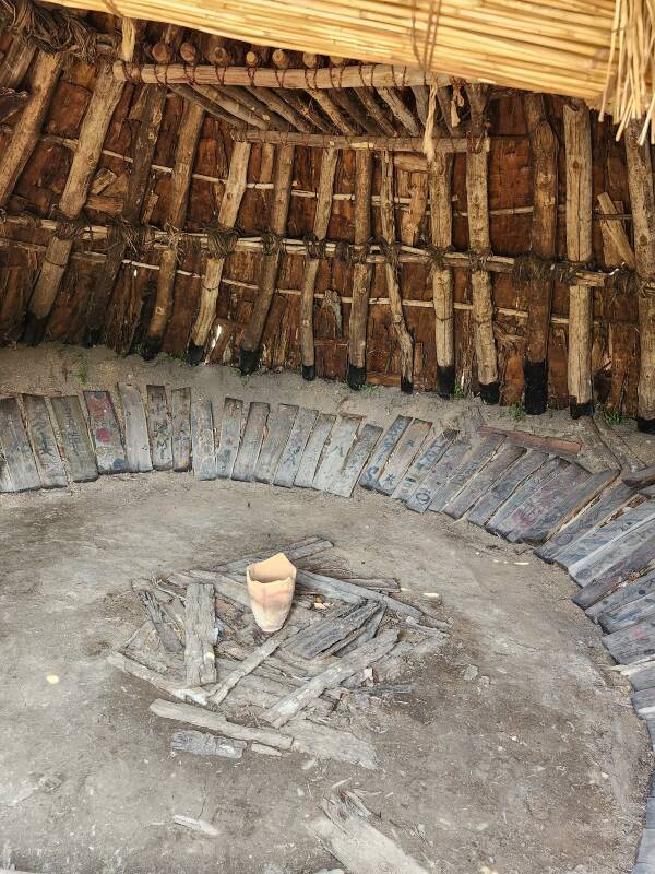 Shallow pit and fire hearth within conical structure built from wood poles and bark pieces.