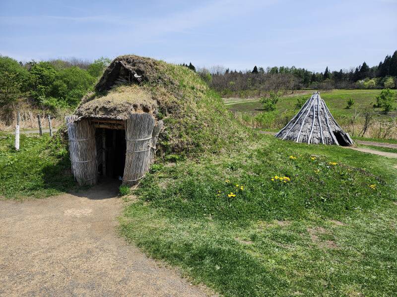 Reconstructed dwelling built from wood poles and thatch bundles, with turf growing over it.