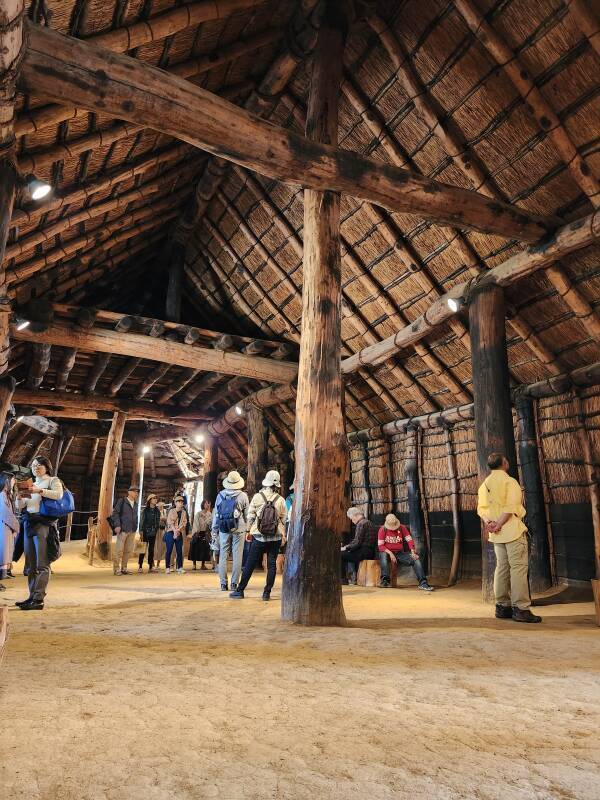 Interior of the largest reconstructed communal structure, large columns, heavy beams, interior of thatch roof overhead, dirt floor.