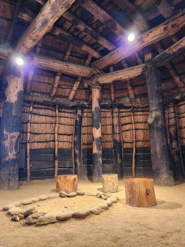 Interior of the largest reconstructed communal structure, large columns, heavy beams, interior of thatch roof overhead, dirt floor.