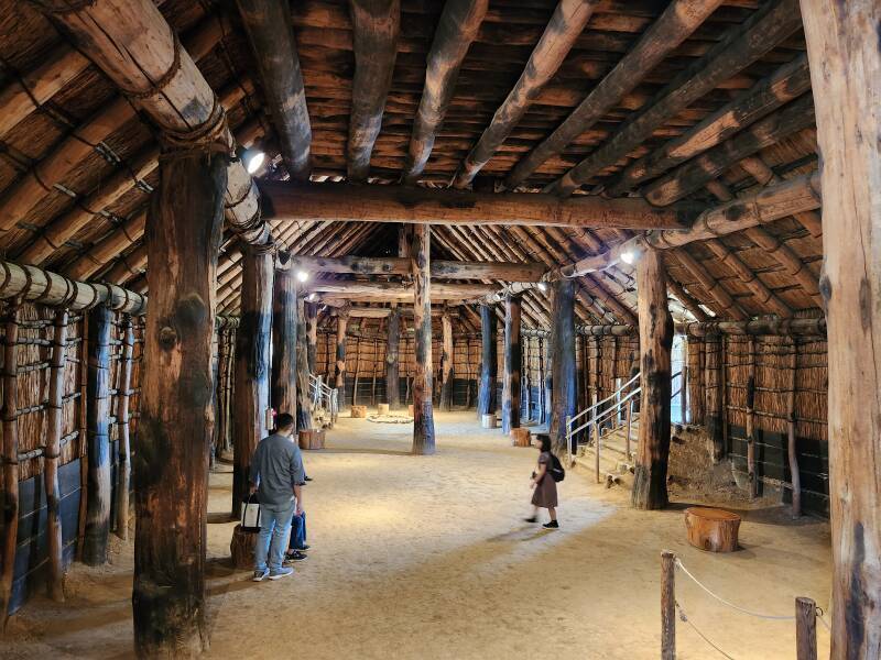 Interior of the largest reconstructed communal structure, large columns, heavy beams, interior of thatch roof overhead, dirt floor.