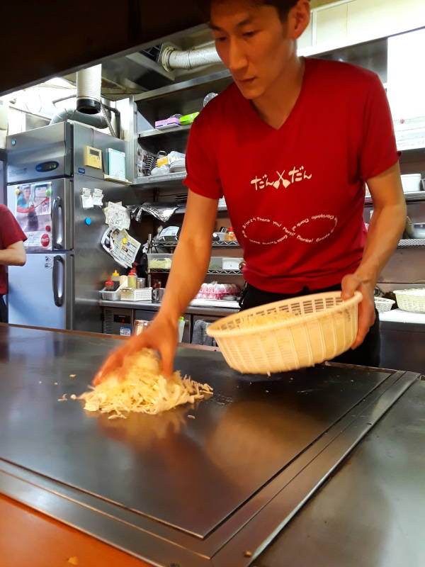 Okonomiyaki chef in Hiroshima, adding shredded cabbage.