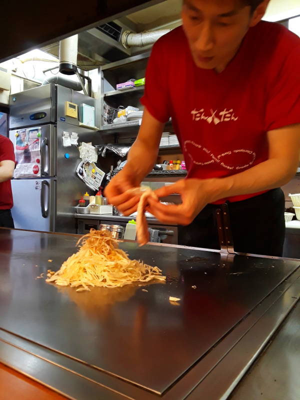 Okonomiyaki chef in Hiroshima, adding bacon.