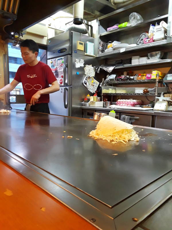Okonomiyaki chef in Hiroshima, flipped over, cooking down.