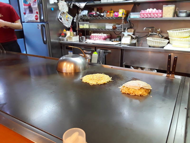 Okonomiyaki cooking in Hiroshima, noodle base and batter layer.
