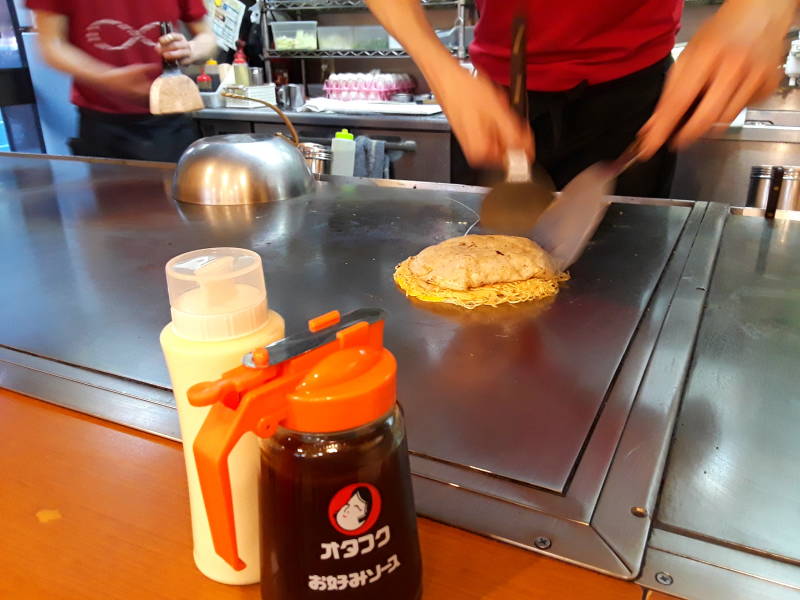 Okonomiyaki chef in Hiroshima, batter, egg, and noodles.