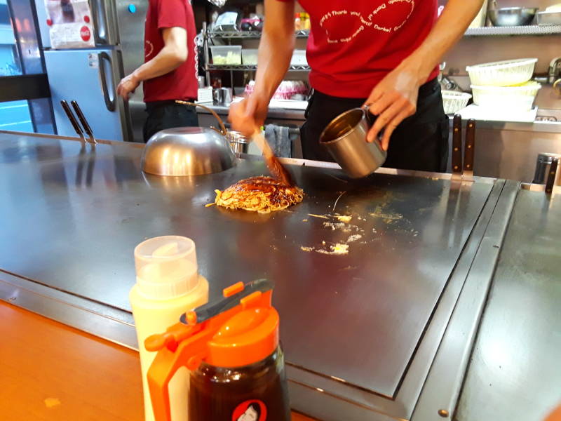 Okonomiyaki chef in Hiroshima, adding more okonomiyaki sauce.