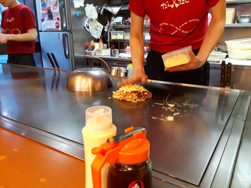 Okonomiyaki chef in Hiroshima, adding mushrooms.